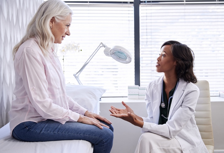 A mature patient in consultation with a dermatologist on an exam couch