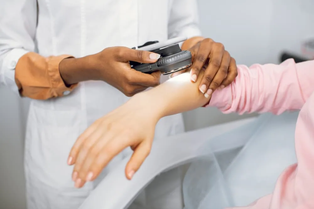 Dermatologist examining patient’s skin with handheld diagnostic device